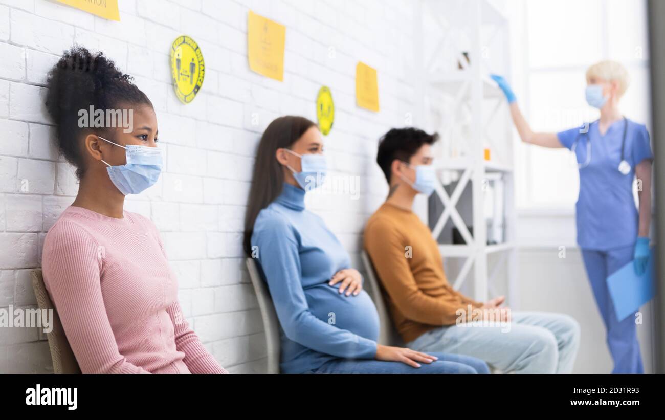 Pazienti con Coronavirus multirazziale seduti in coda in attesa di appuntamento in ospedale Foto Stock