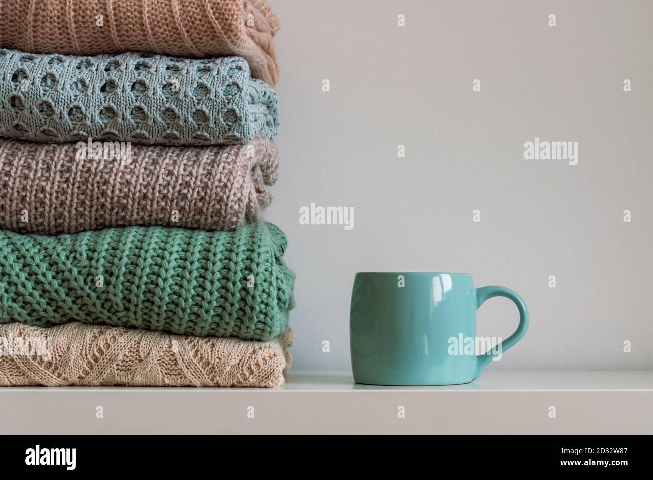 Pila di maglioni da donna a maglia calda e tazza di bevanda calda su sfondo bianco. Concetto di autunno o inverno Foto Stock