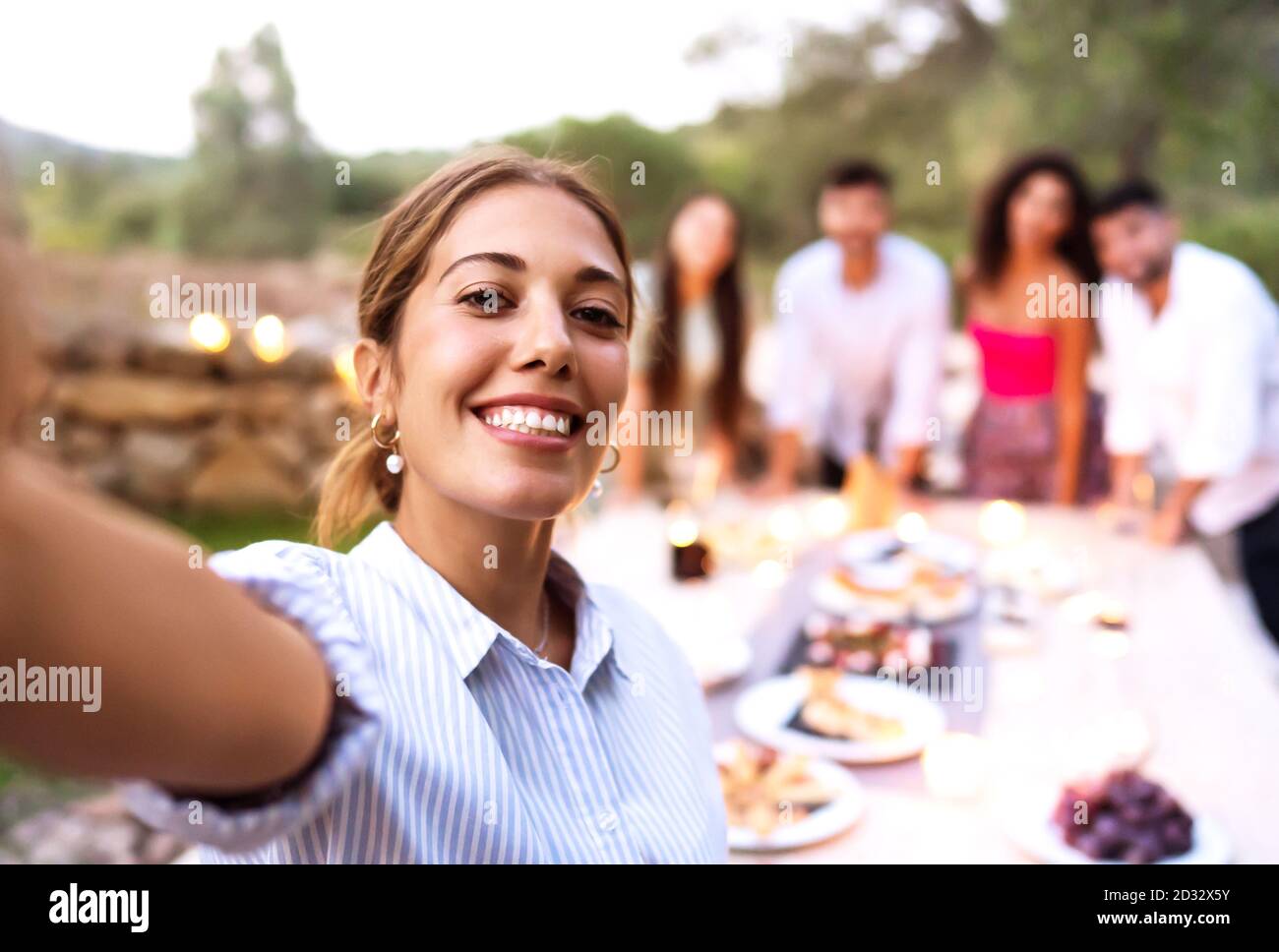 Carino giovane donna sorridente fare un auto-ritratto di se stessa e. amici sullo sfondo festeggiando in giardino al tramonto - buon momento di amici di a. Foto Stock