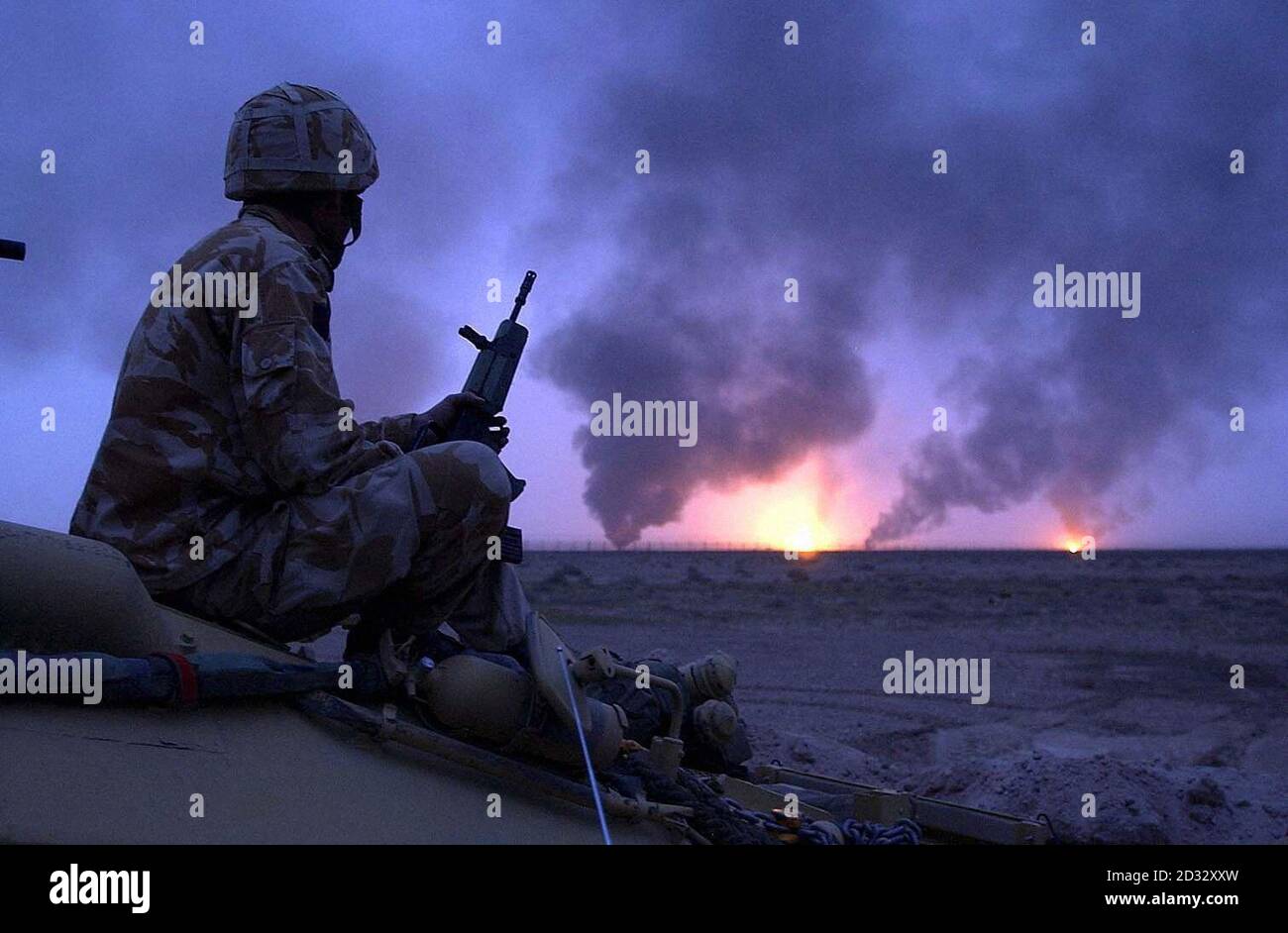 Il petrolio è incendiato nell'Iraq meridionale, mentre un soldato britannico guarda sopra. Foto Stock