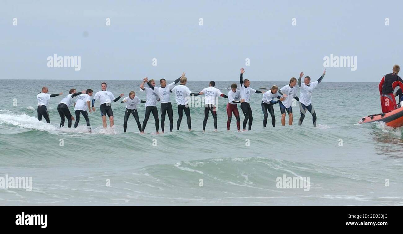 Quattordici record breakers durante il loro quarto tentativo su una tavola da surf per ottenere il record mondiale a St Ives, Cornovaglia. Un team di 14 persone ha fatto il pieno di record mondiali guidando un'onda su una singola tavola da surf gigante. * l'offerta record è stata tenuta a St Ives, Cornovaglia occidentale su una tavola di 37 piedi del peso di 400 libbre. Al quarto tentativo, la squadra di 12 uomini e due donne si alzò e si surfò in riva insieme, stabilendo il primo record mondiale ufficiale per il maggior numero di persone che cavalcavano una sola tavola. Foto Stock