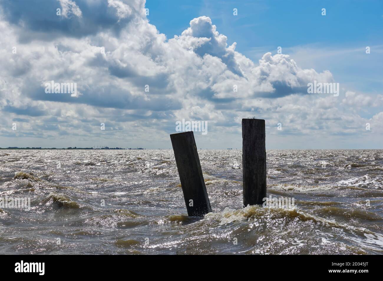 Due poli in un mare turbolento sotto un cielo blu con grandi nuvole. Vista sul mare di Wadden vicino a Holwerd nei Paesi Bassi. Foto Stock