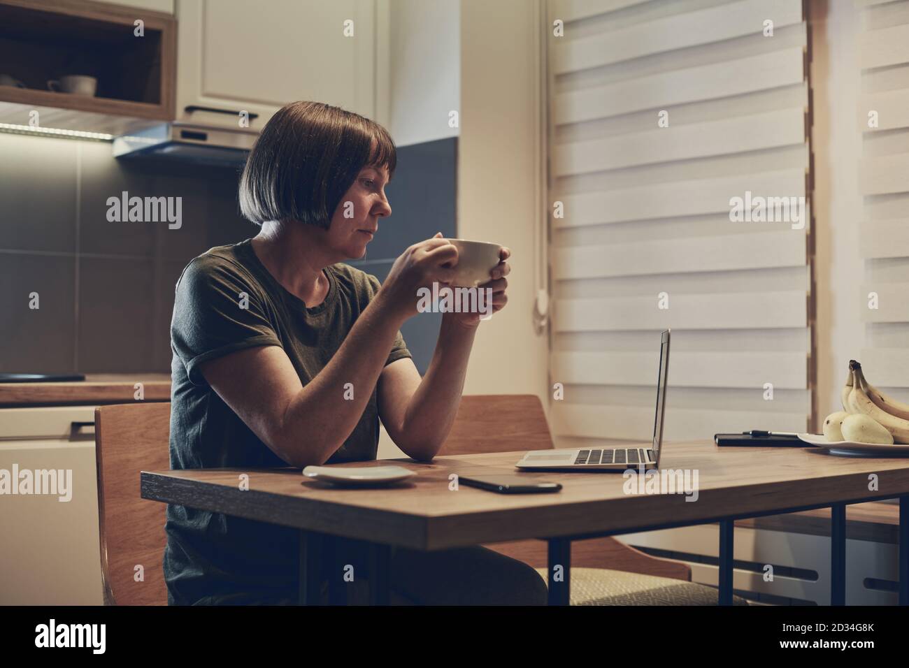 Donna freelance che lavora da casa a tarda notte e beve caffè guardando lo schermo del computer portatile Foto Stock