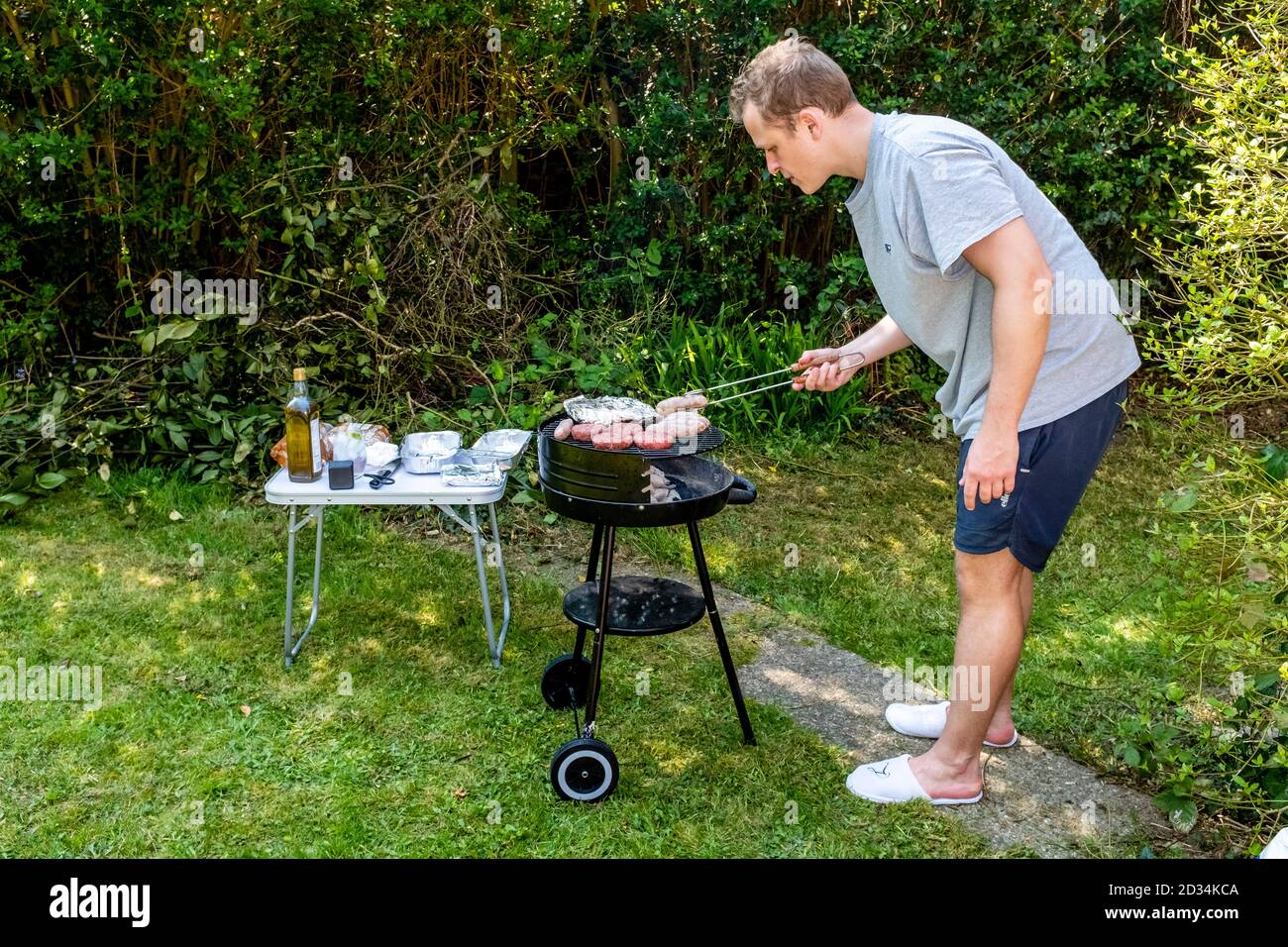 Un giovane uomo che cucina cibo su UN barbecue, Sussex orientale, Regno Unito. Foto Stock