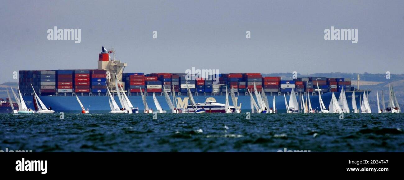 Una nave container passa gli yacht che corrono sul Solent il giorno di apertura della regata della Skandia Cowes Week al largo di Cowes, Isola di Wight. Foto Stock