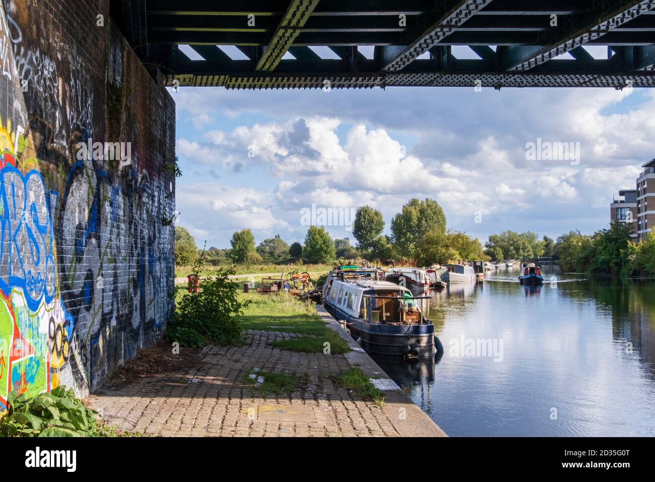Regno Unito, Londra. Paesaggio urbano - case galleggianti sul fiume Lea navigabile sezione canale con graffiti sotto un ponte ferroviario e un cielo estivo limpido Foto Stock