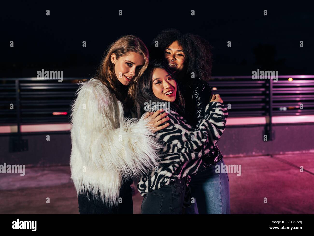 Tre belle fidanzate che si abbracciano mentre si levano in piedi sul tetto alle luci al neon Foto Stock