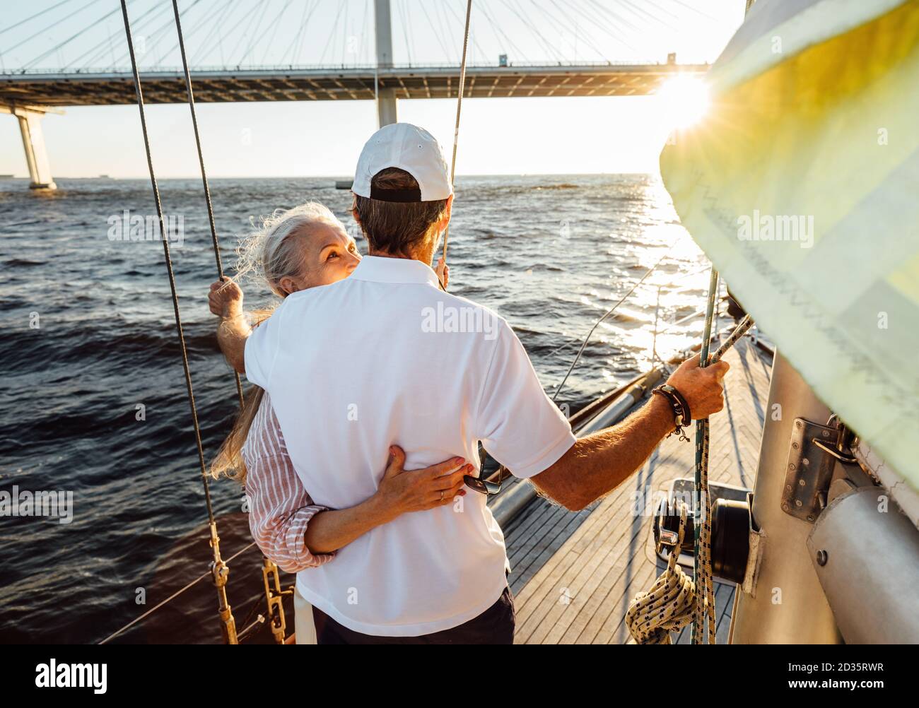 Vista posteriore di una coppia anziana abbracciata su un privato yacht e guardando in lontananza Foto Stock