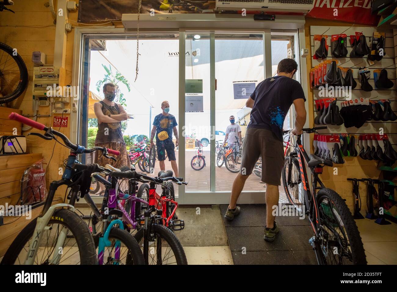 Negozio di biciclette durante il COVID-19 Pandemic. I clienti aspettano fuori dal piccolo negozio per il servizio e vengono serviti alla porta. I clienti sono obbligati a wea Foto Stock