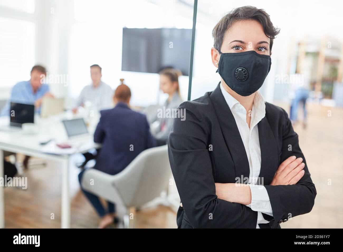 Donna di affari fiduciosa con maschera facciale e braccia incrociate dentro l'ufficio Foto Stock