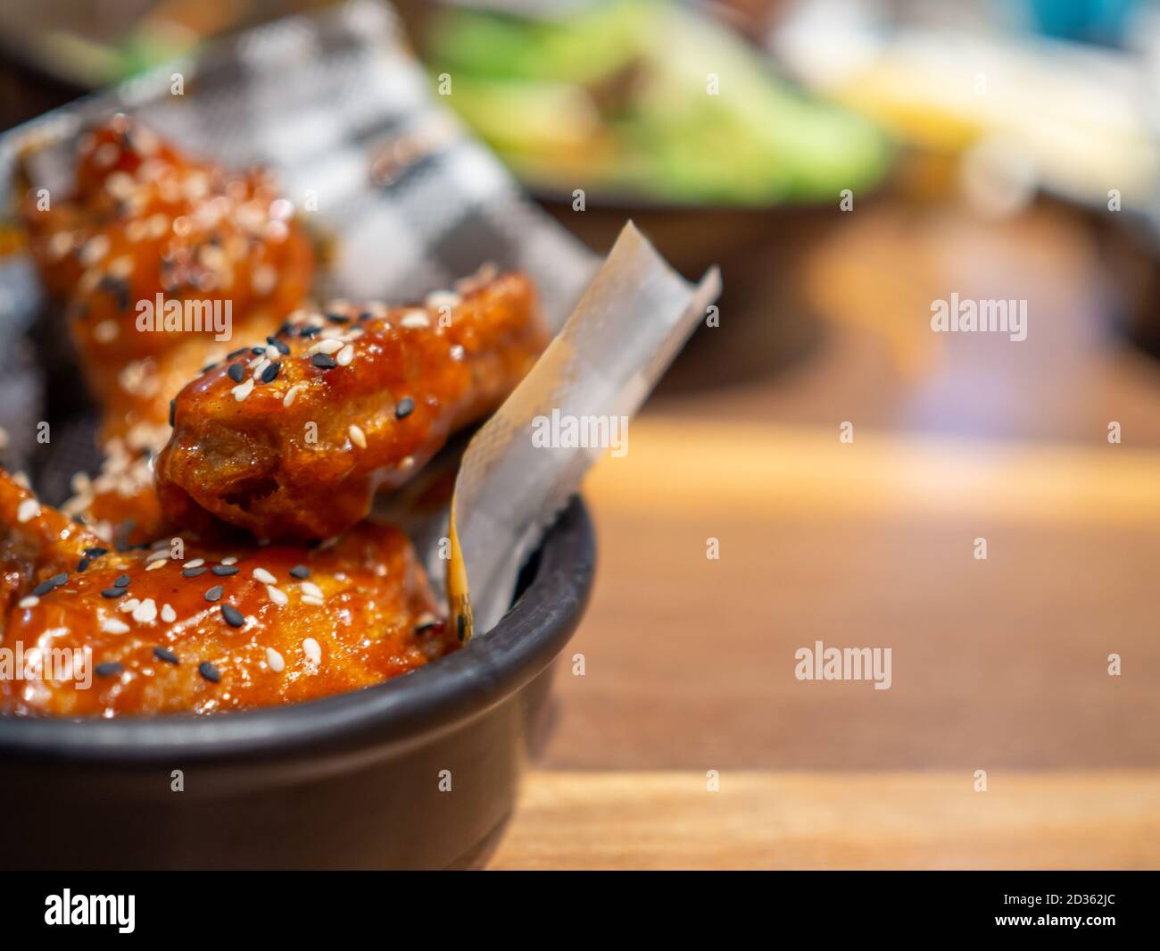 Pollo al barbecue coreano su un piatto nero posto su un tavolo di legno e con uno sfondo sfocato. Foto Stock