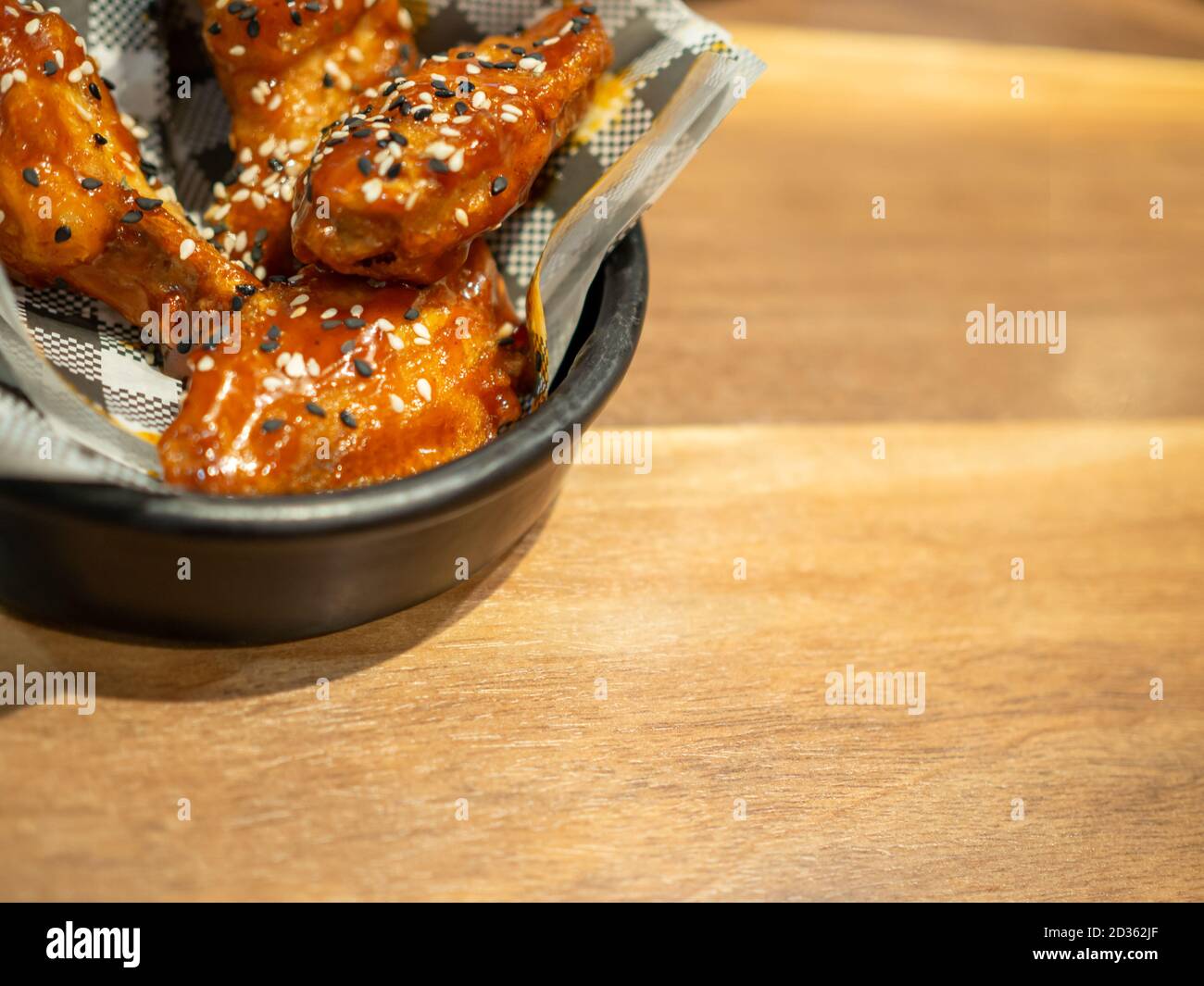 Pollo al barbecue coreano su un piatto nero posto su uno sfondo di tavolo di legno. Foto Stock