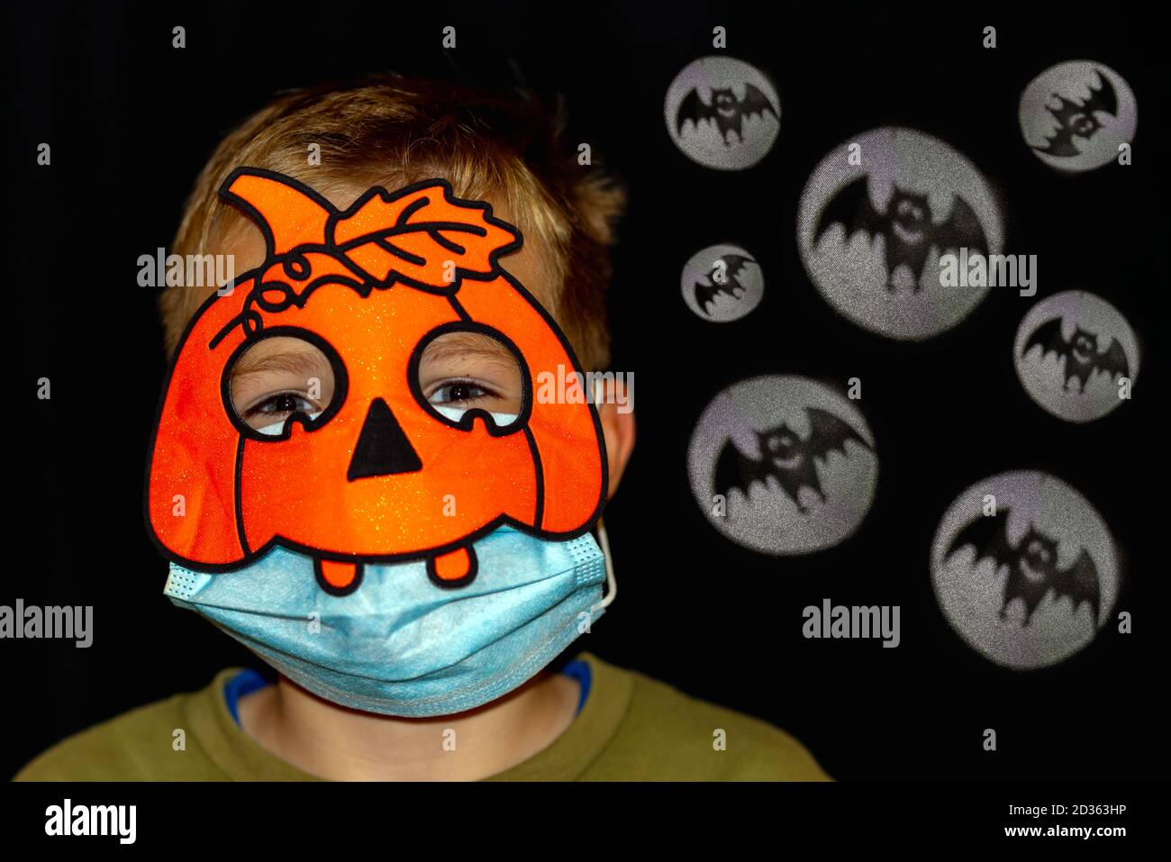 Vista frontale primo piano decorazioni di Halloween in nuova realtà della pandemia COVID-19. Ragazzo in zucca arancione maschera medica blu.UN sacco di riflettore con pipistrello si Foto Stock