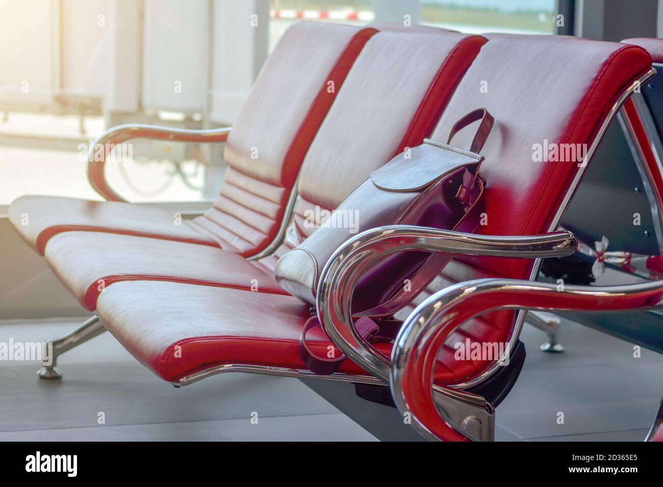 Tre sedie rosse vuote nella lounge dell'aeroporto e in borgogna primo piano dello zaino in pelle da donna Foto Stock