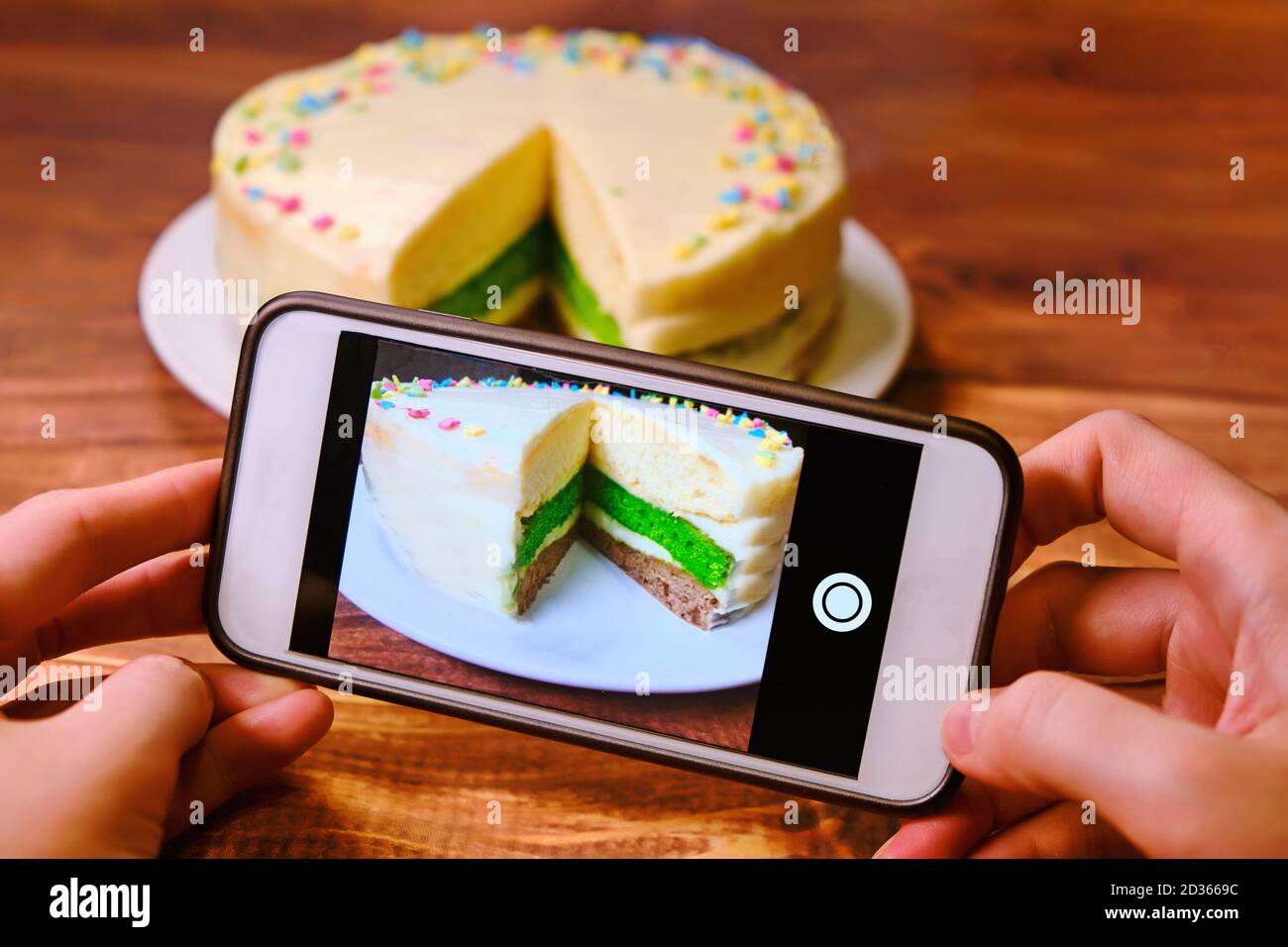 Le mani delle donne con il telefono che scatta le foto della torta. Blogger spara cibo per instagram. Creare una foto per la pubblicazione su Internet. Telefono bianco a Foto Stock