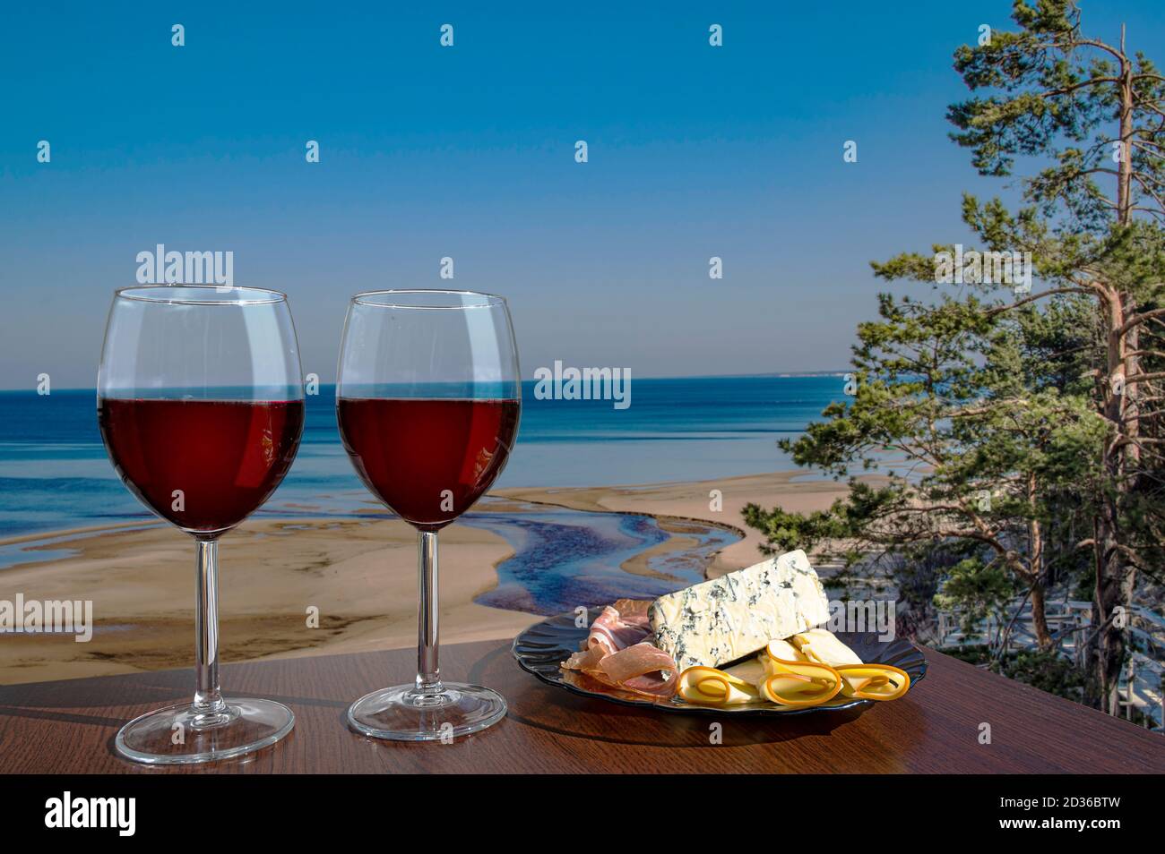 Due bicchieri di vino con assortimento di salumi contro la vista della spiaggia e Mar Baltico in primavera, Estonia. Spiaggia con sabbia bianca e mare blu/oceano. Foto Stock