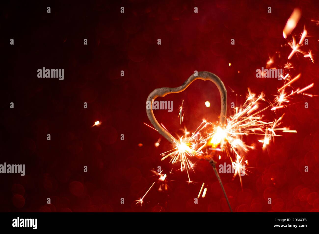 Forma del cuore la luce del Bengala si illumina su sfondo astratto rosso. Biglietto d'auguri per le vacanze, sfondo per San Valentino e il giorno del matrimonio. Metafora romantica conc Foto Stock