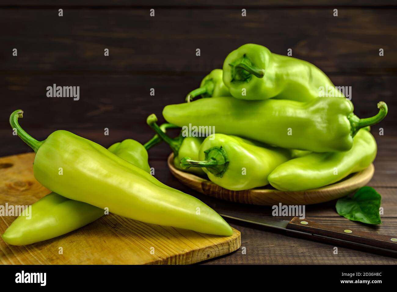 Peperoni verdi dolci su un tagliere, piatto con peperoni e coltello da cucina su tavola di legno. Messa a fuoco selettiva. Foto Stock