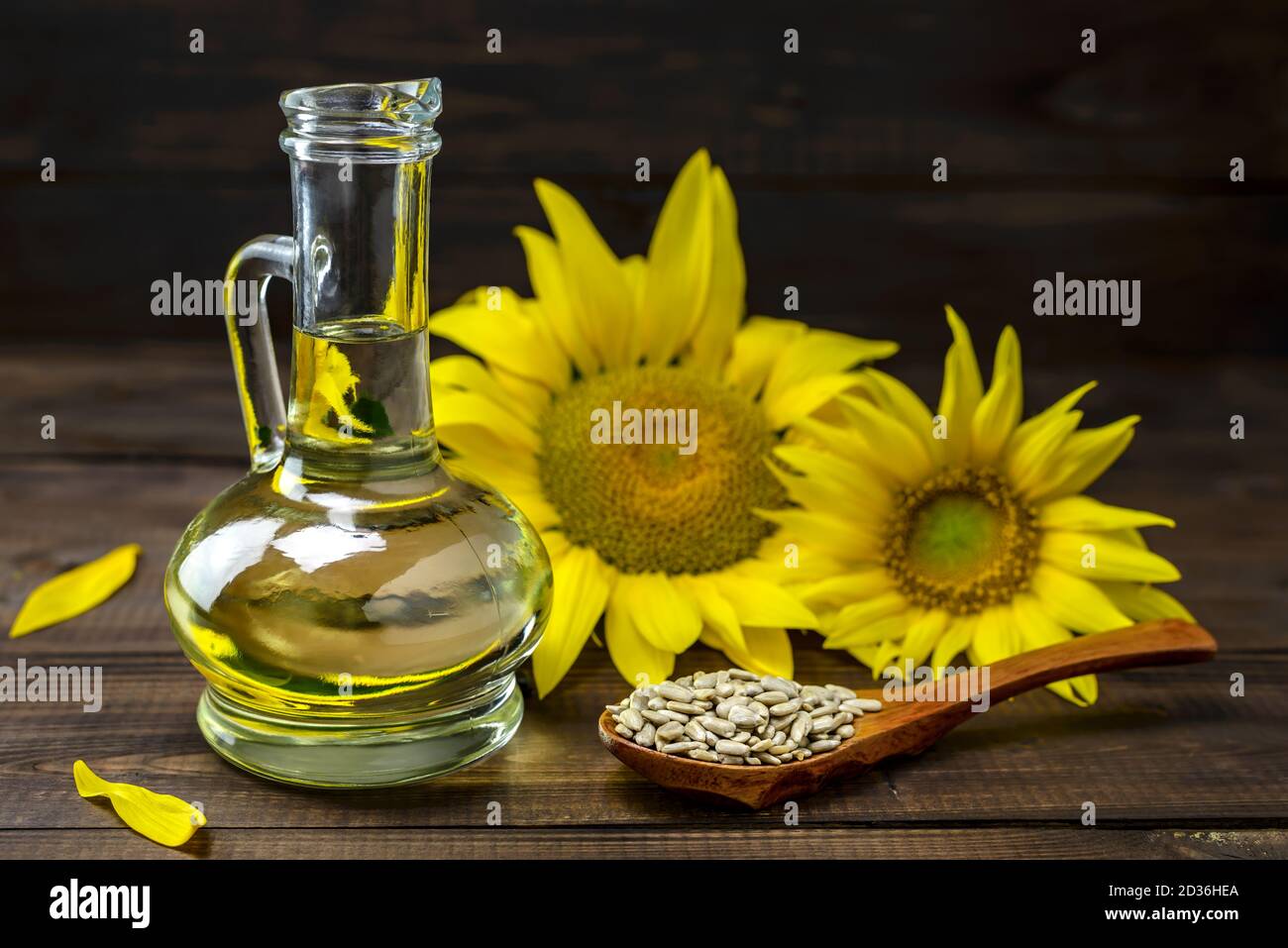 Olio di girasole in bottiglia e semi di girasole sbucciati su un cucchiaio di legno vicino a un fiore di girasole fresco su sfondo di legno. Messa a fuoco selettiva. Foto Stock