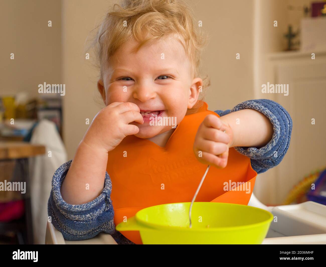 Felice bambino di un anno sorridente mangiando con le posate a casa Foto Stock