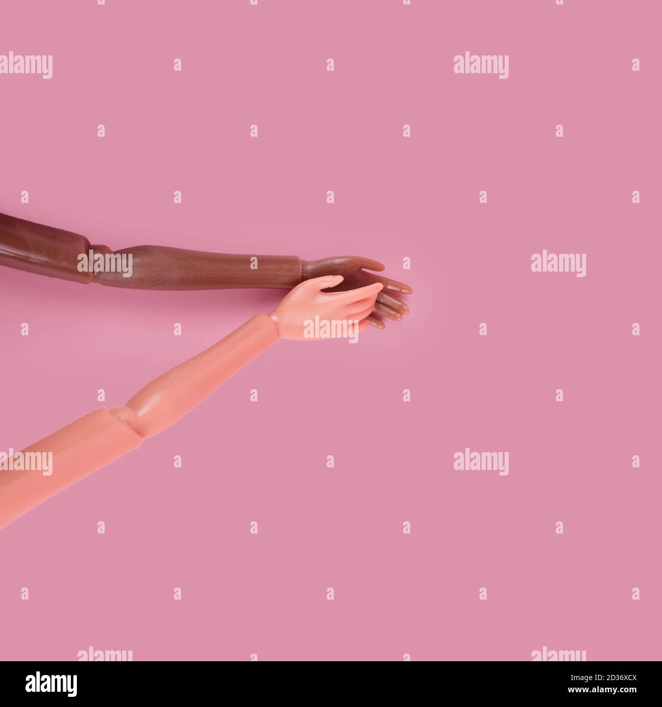 Due mani di bambola si raggiungono l'una per l'altra su sfondo rosa. Diverse tonalità della pelle e razze. Fermare il razzismo, la diversità e l'unità, l'uguaglianza e il femminismo Foto Stock