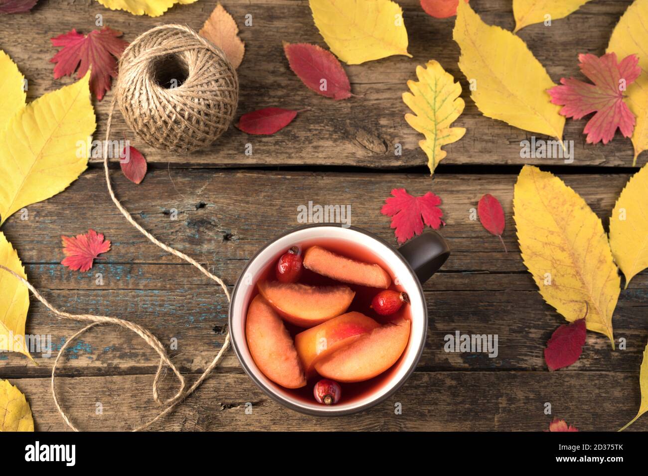 Tazza con tè caldo con frutta e fianchi di rose su sfondo naturale di legno con foglie d'autunno. Foto Stock