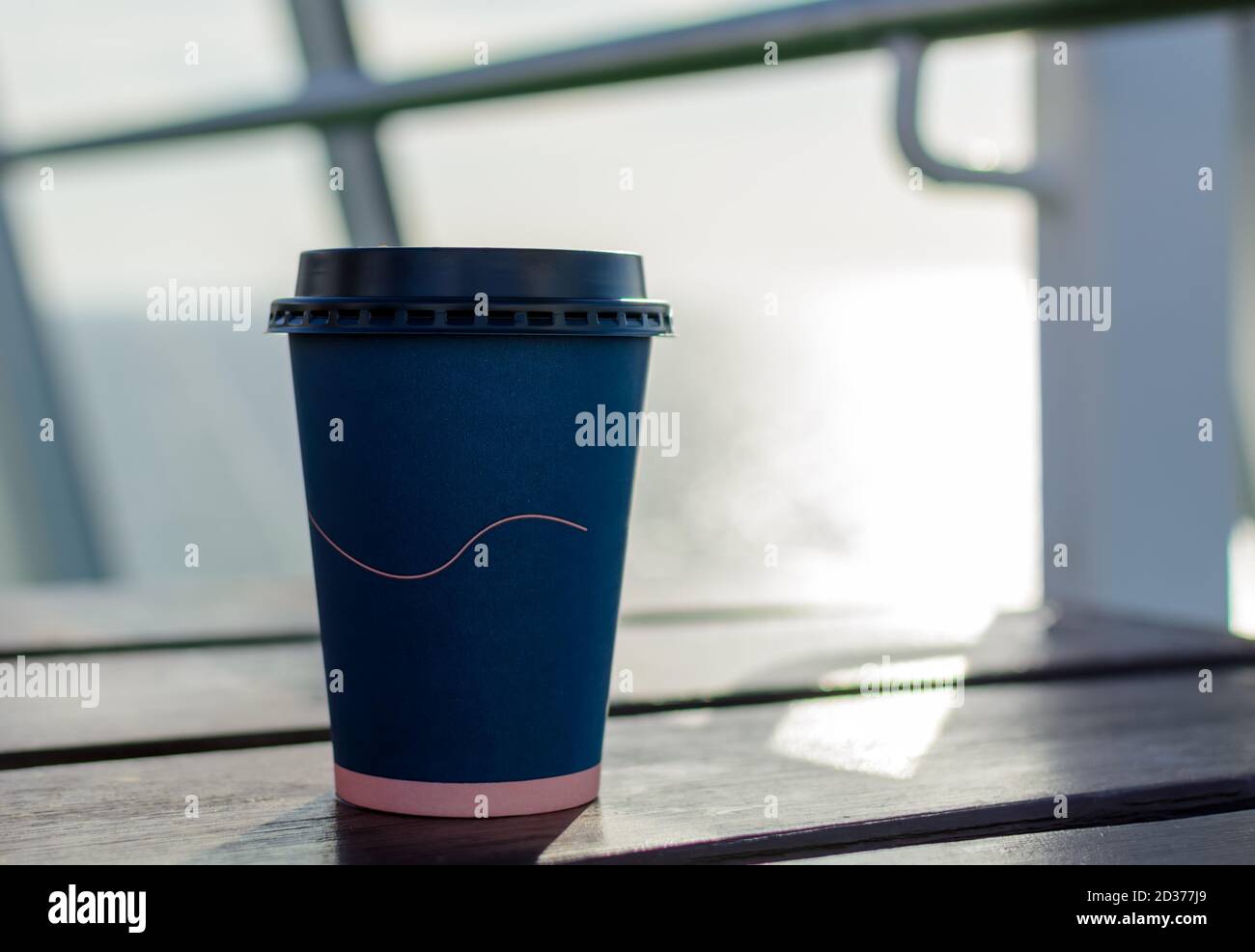 Tazza da caffè di carta monouso blu scuro con coperchio in plastica nera su tavolo di legno alla nave da crociera Foto Stock