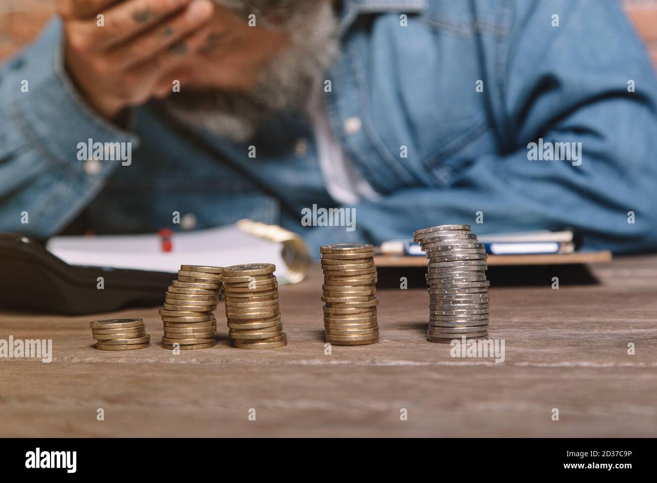 Uomo alla scrivania in camicia in denim che tiene la testa e preoccupandosi per i soldi. Foto Stock