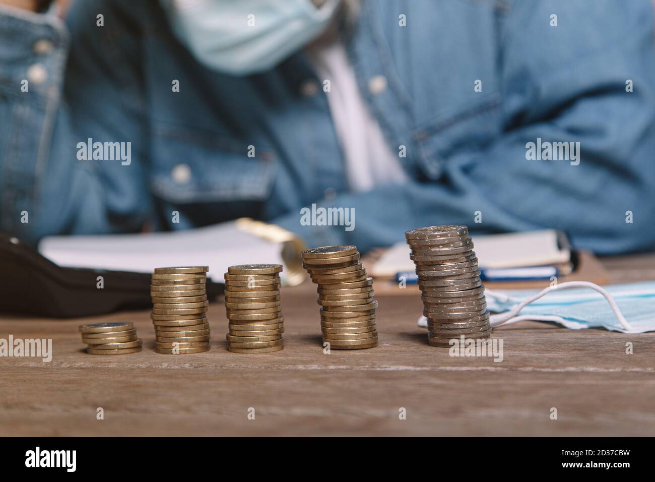 Uomo alla scrivania in camicia denim e maschera di tenuta testa frustrato dal denaro. Foto Stock