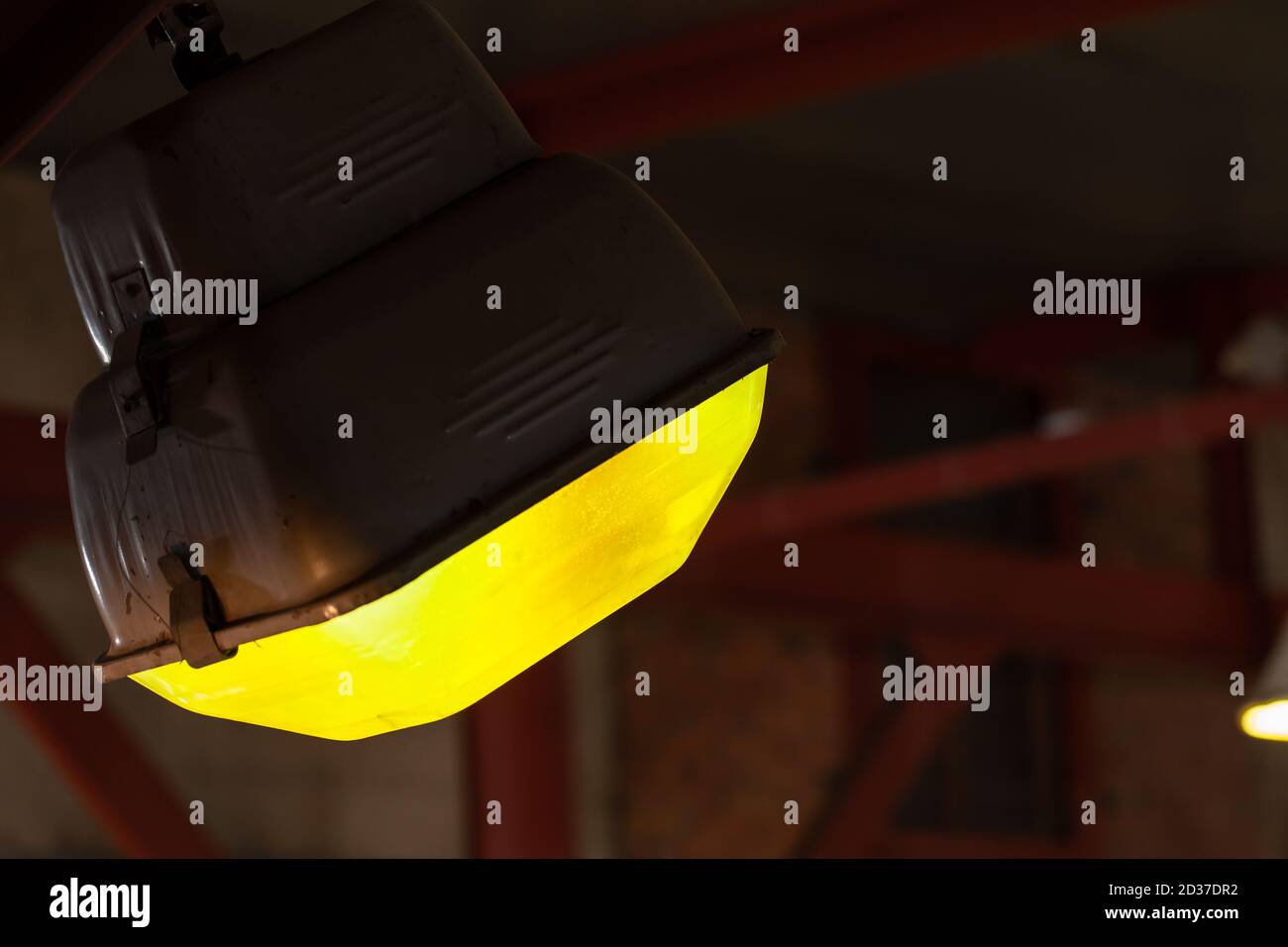 Luce industriale gialla montata sul soffitto che illumina gli interni scuri, foto in primo piano con messa a fuoco selettiva Foto Stock