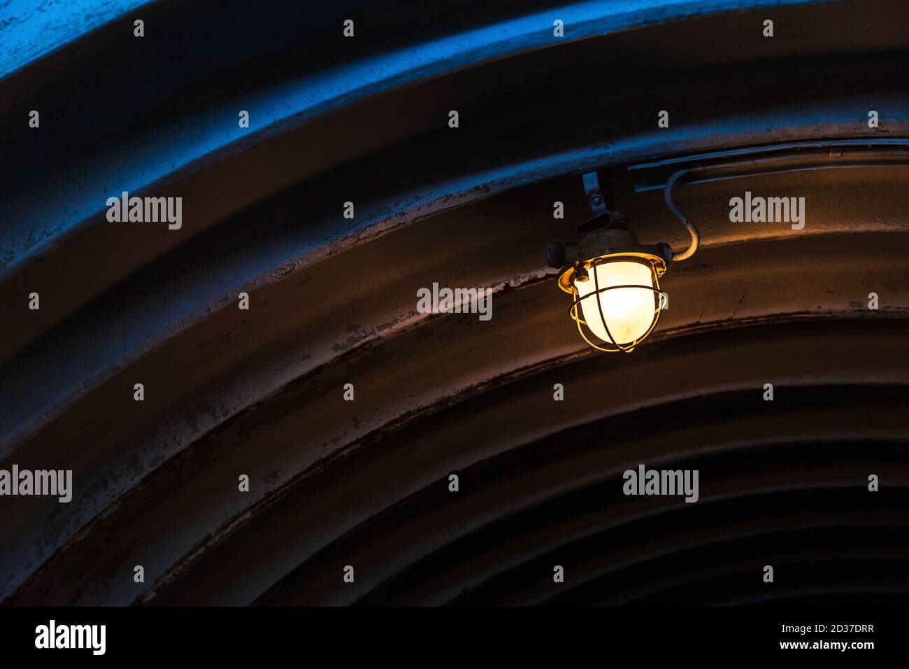 Luce industriale con lampada al tungsteno montata su una parete in metallo che si illumina in un tunnel scuro, foto in primo piano con messa a fuoco selettiva Foto Stock