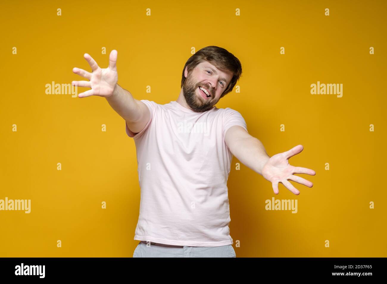 Gioioso, sorridente, l'uomo bearded allunga le braccia per un abbraccio. Benvenuto. Sfondo giallo. Foto Stock