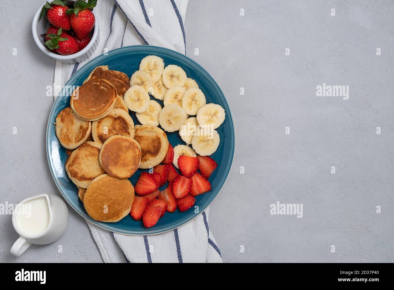 Colazione casalinga alla moda con mini pancake e fragola su sfondo grigio neutro. Vista sopra con spazio per la copia Foto Stock