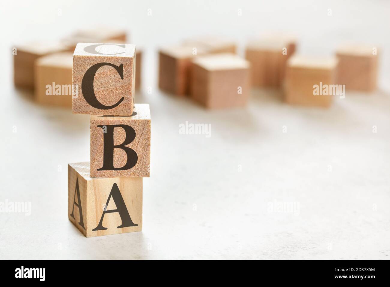Tre cubetti di legno con lettere CBA (valutazione costi/benefici), su tavola bianca, più sullo sfondo, spazio per il testo nell'angolo in basso a destra Foto Stock