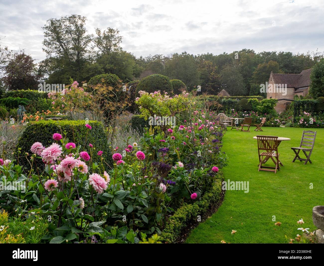 Chenies Manor giardini nel mese di settembre. Dahlias rosa 'Karma Prospero', 'barra' Rose Ballerina nel lungo confine erbaceo, prato con sedie da giardino. Foto Stock