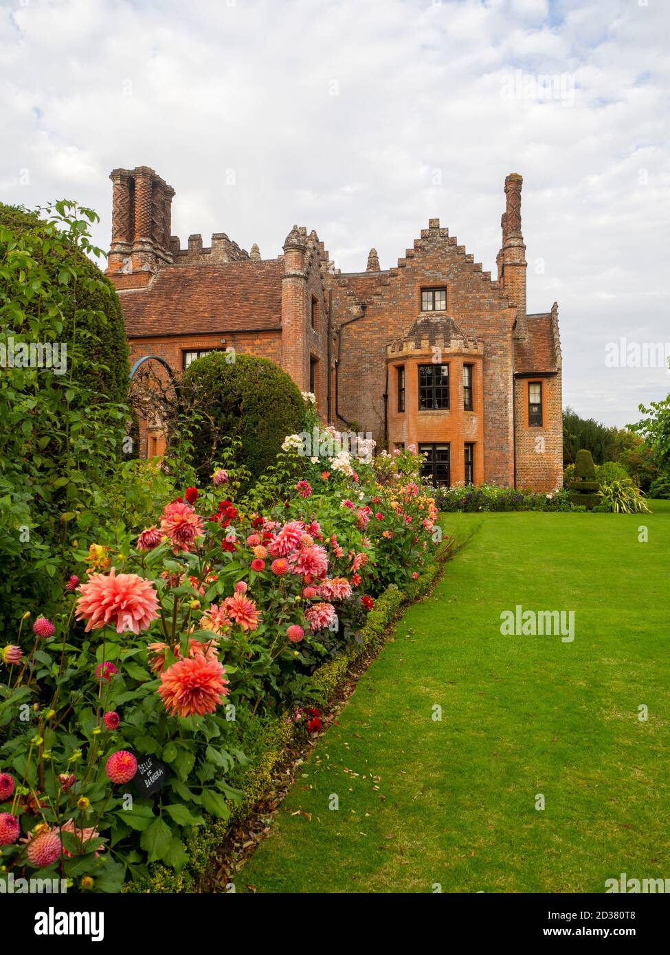 Splendidi giardini Chenies Manor a settembre circondati da fiori di dahlias rosa salmone, 'Belle of Barmera', alberi di tasso tagliati e Rosa 'Ballerina'. Foto Stock