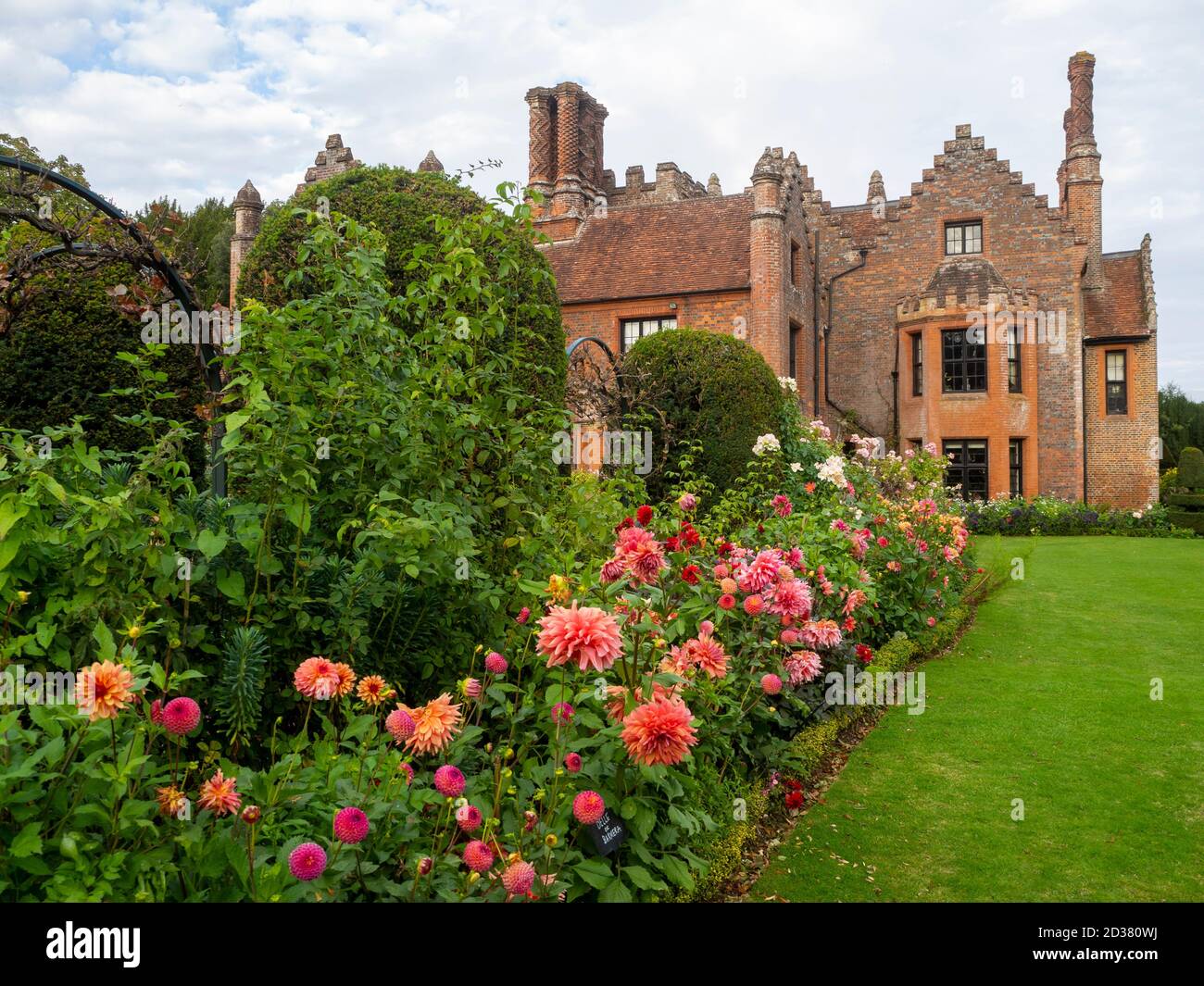 Chenies Manor giardini nel mese di settembre. Splendida pesca e salmone rosa Dahlia mostra con il Tudor Manor come sfondo in un bel pomeriggio in tarda estate. Foto Stock