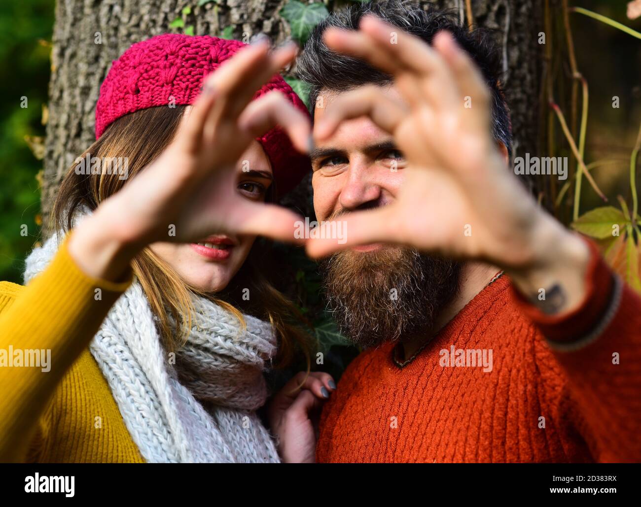 Coppia innamorata mostra il segno del cuore con le dita. Uomo e donna con  volti sorridenti su sfondo albero. Datazione e concetto d'amore d'autunno.  Ragazza in cappello rosa e ragazzo sopportato o