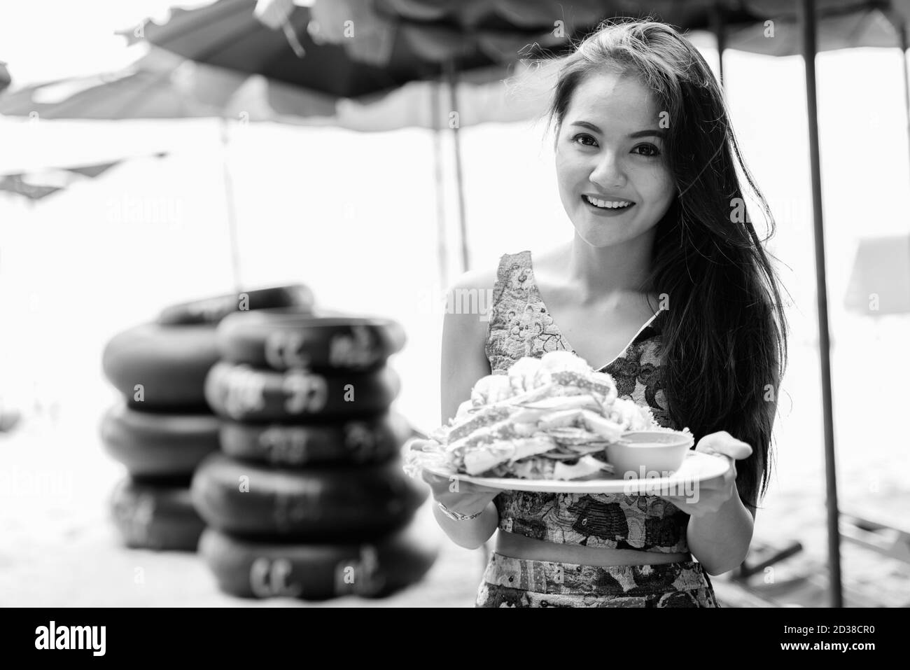 Giovane felice bella donna asiatica sorridente mentre tiene piatto di granchi cotti al vapore sulla spiaggia Foto Stock