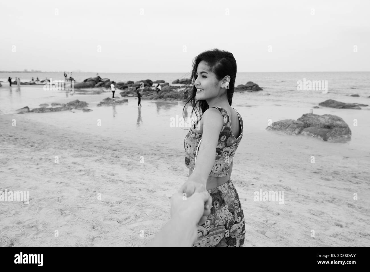 Premurosa giovane donna asiatica felice sorridente mentre tiene le mani e. uomo leader in spiaggia Foto Stock