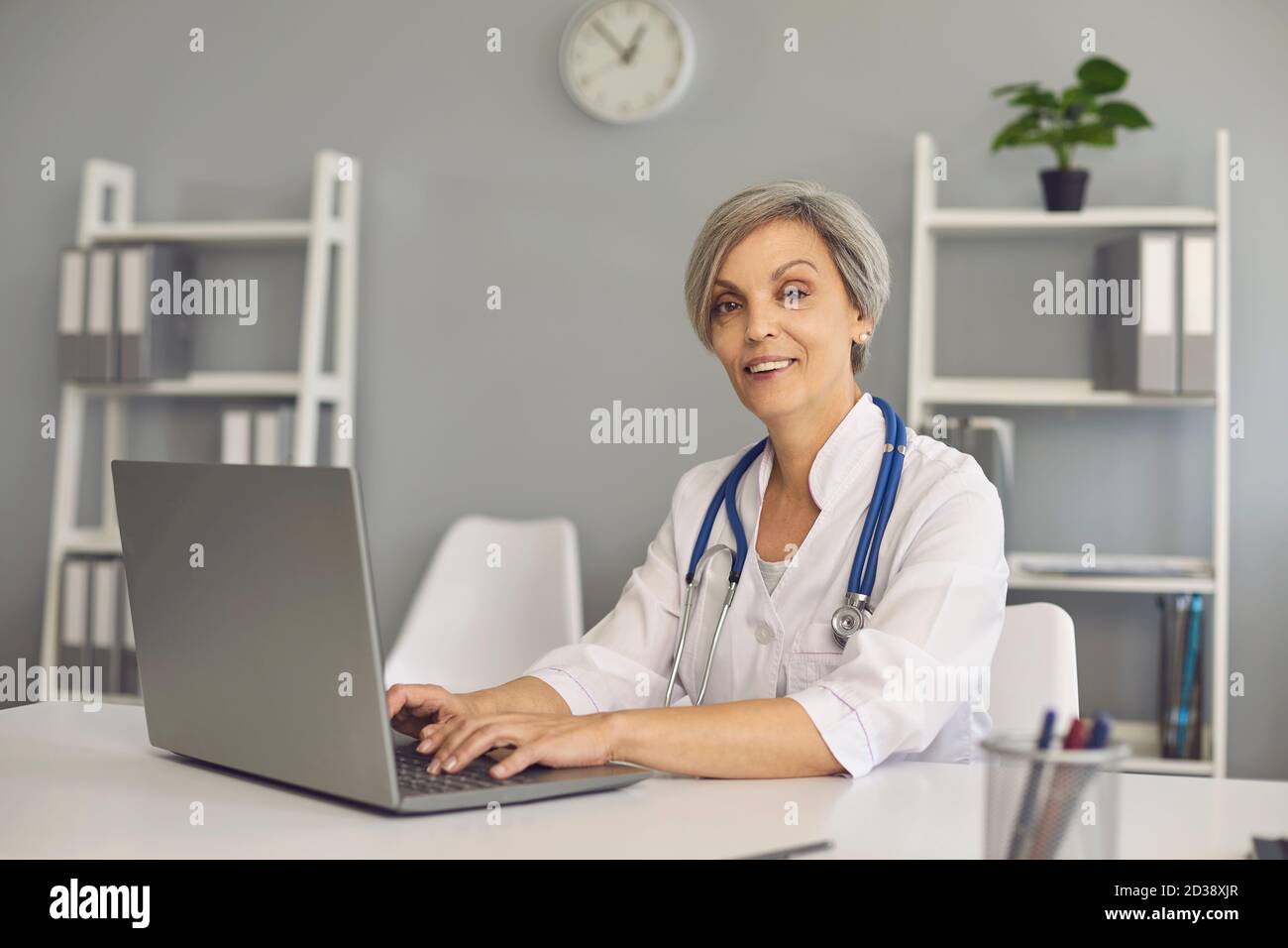 Portert positivo matrue dottore donna con computer portatile in clinica. Medico online. Foto Stock