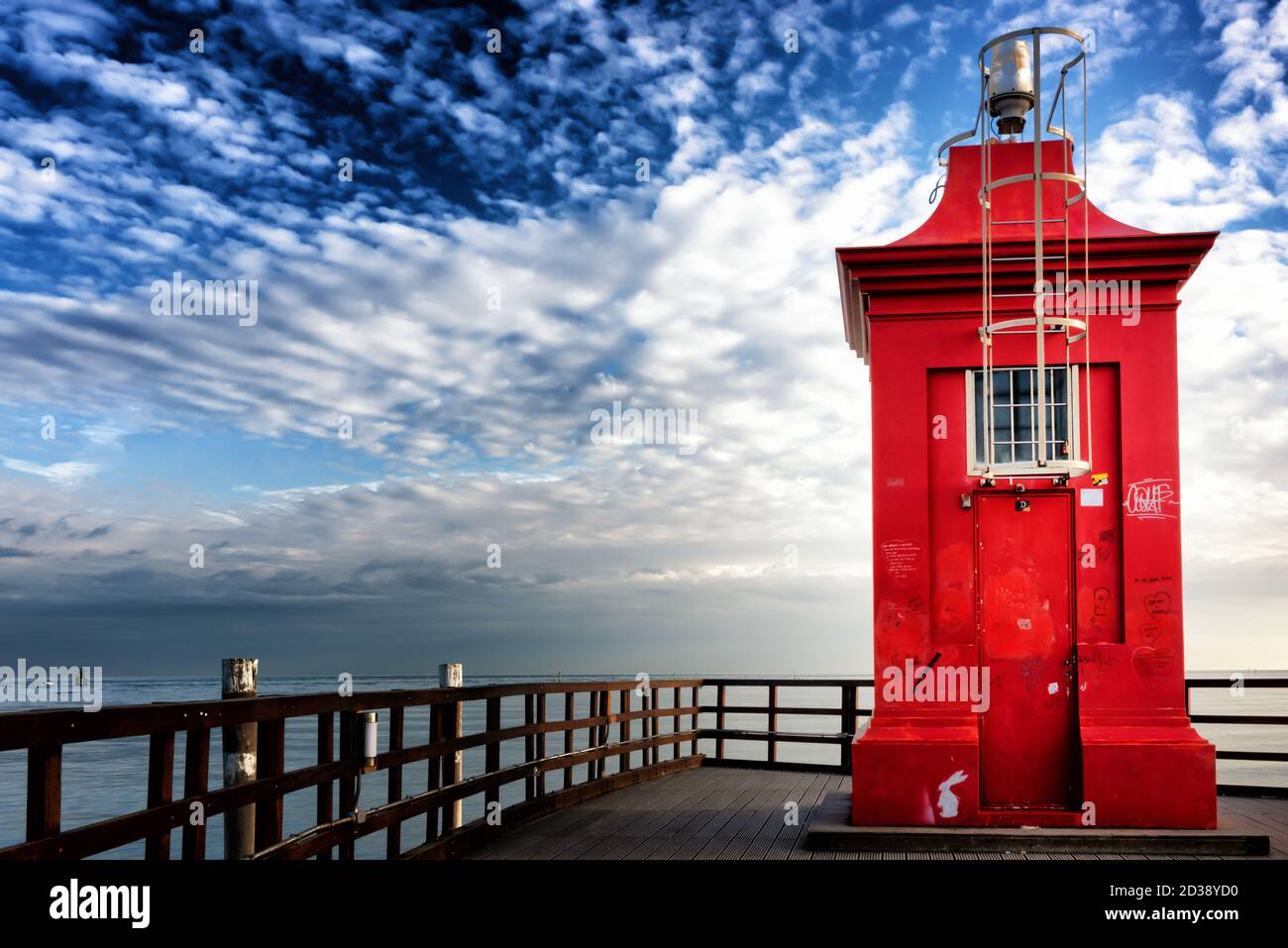 Piccolo faro rosso su un molo di legno sotto un cielo suggestivo. Lignano Sabbiadoro, Friuli Venezia Giulia, Italia. Foto Stock