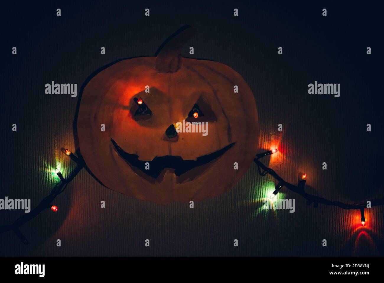Una zucca di carta con una ghirlanda lampeggiante al posto degli occhi, appesa alla parete. Un modello orribile per Halloween. Foto Stock