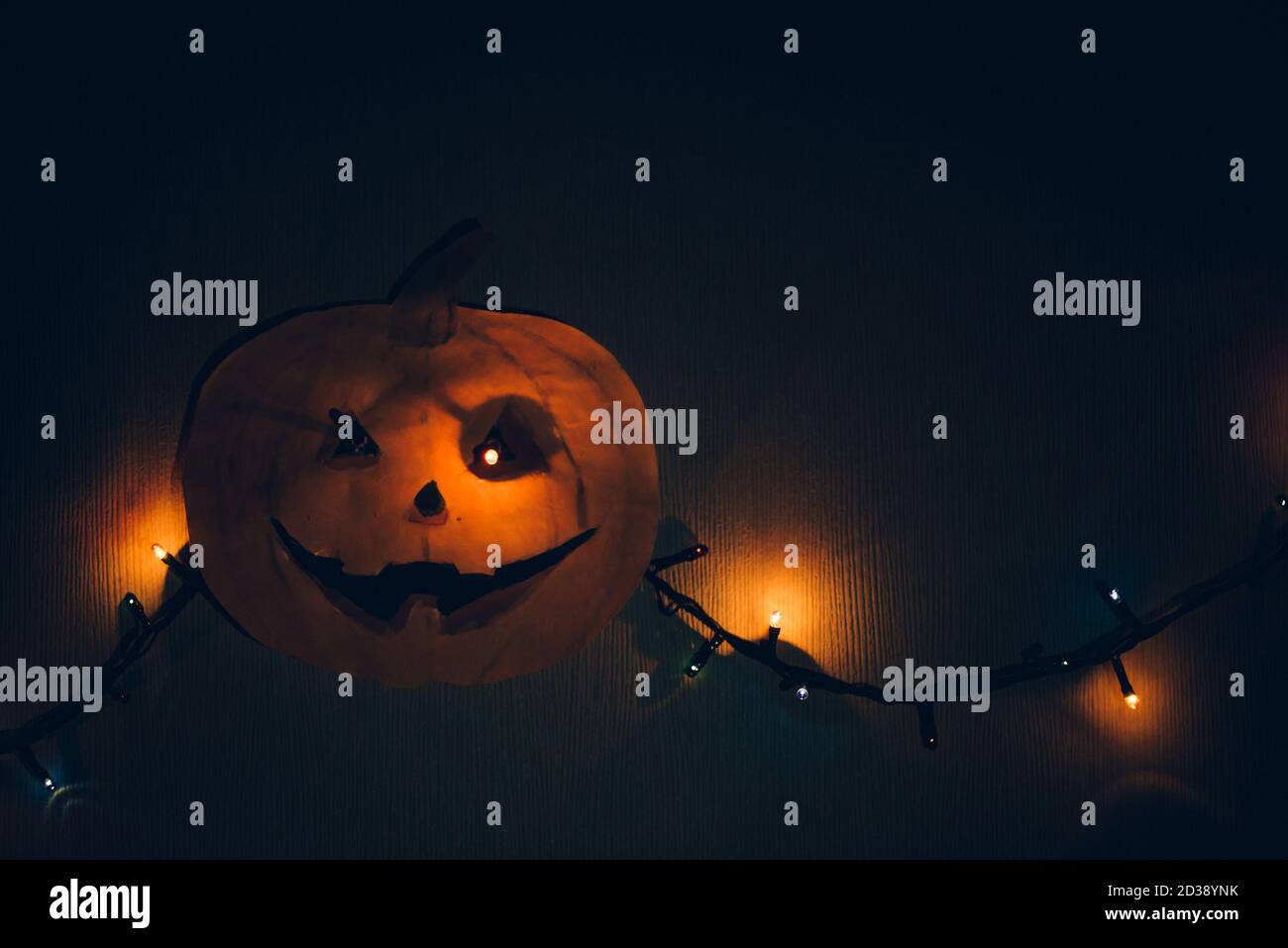 Una zucca di carta con una ghirlanda lampeggiante al posto degli occhi, appesa alla parete. Un modello orribile per Halloween. Foto Stock