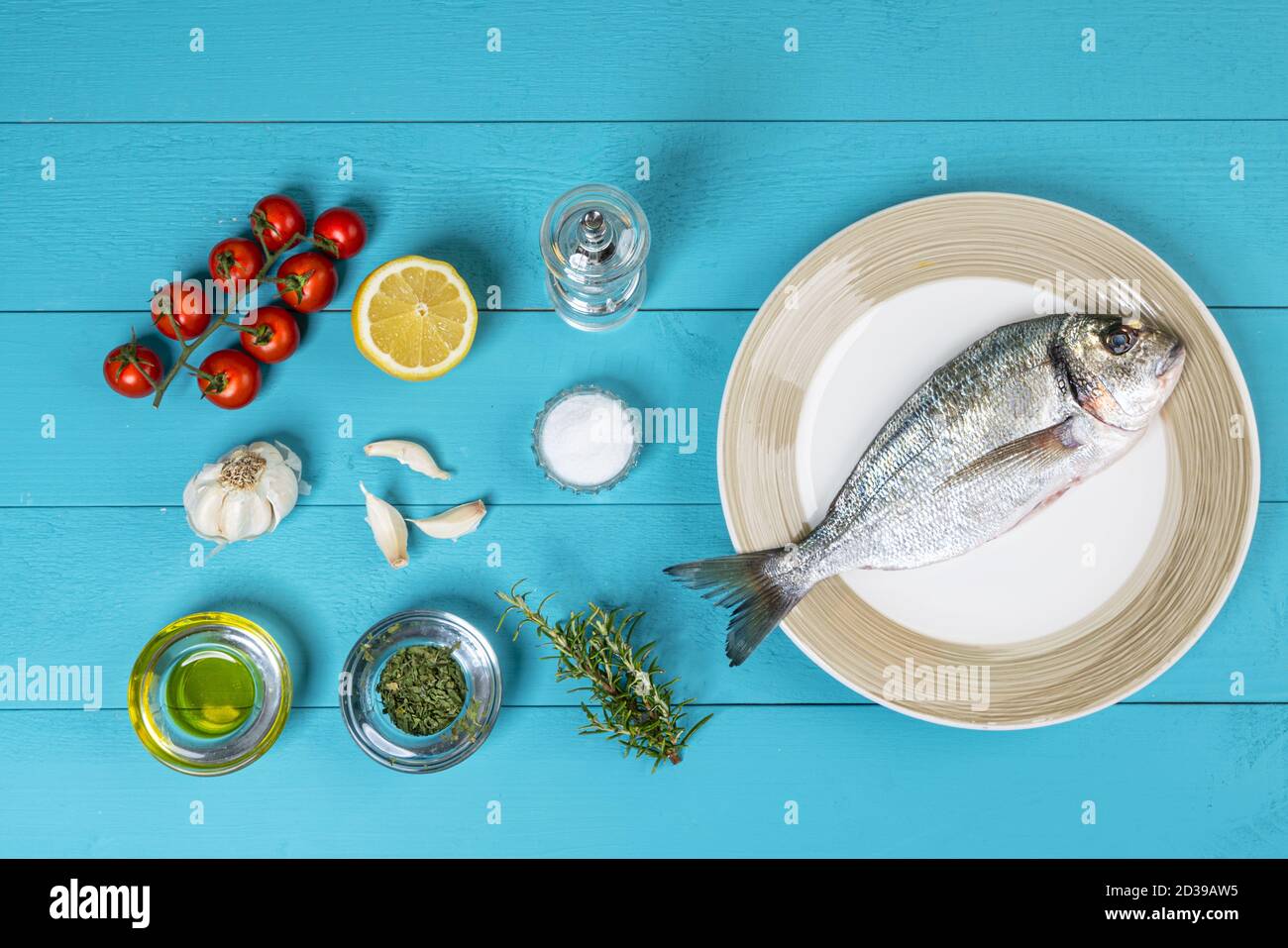 una orata di mare e con prodotti per la preparazione di una ricetta su un tavolo di legno blu Foto Stock