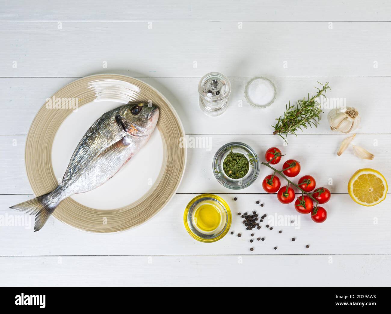 una orata di mare e con prodotti per la preparazione di una ricetta su un tavolo di legno bianco Foto Stock