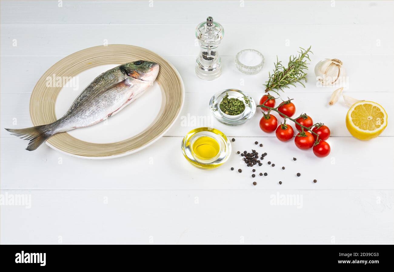 una orata di mare e con prodotti per la preparazione di una ricetta su un tavolo di legno bianco Foto Stock