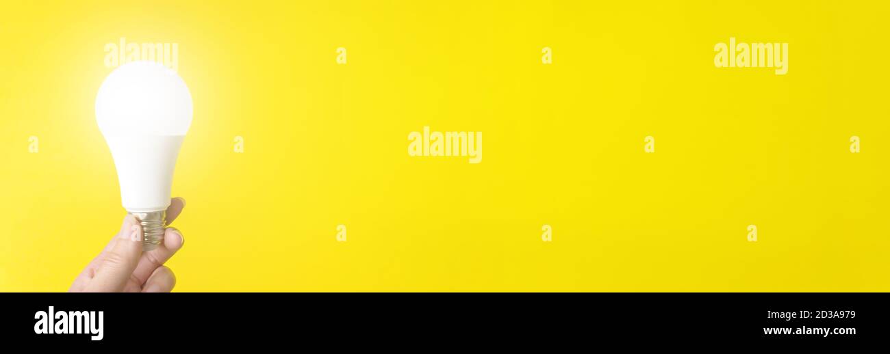 Lampada illuminata con supporto manuale su sfondo giallo. Formato banner Foto Stock