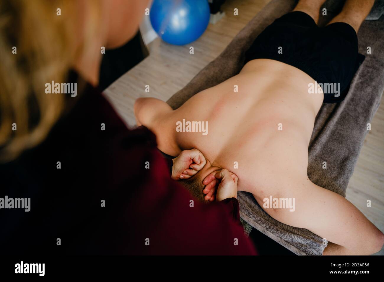 Fisioterapista massaggiante la colonna vertebrale superiore del paziente maschile sdraiato a letto in studio di massaggio sportivo. Foto Stock