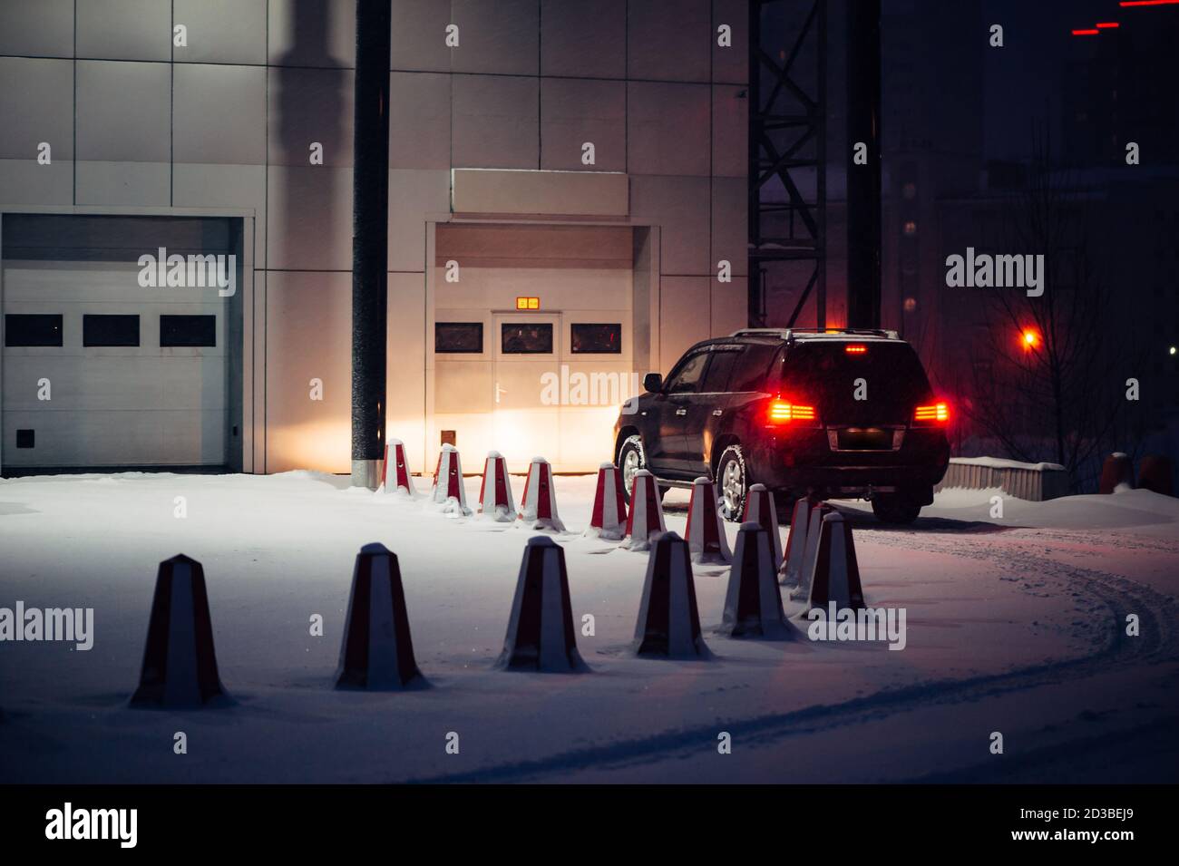 L'auto nera fuori strada chiama il cancello automatico per la manutenzione la sera d'inverno. Macchina parcheggiata vicino all'edificio dell'ufficio. Automobile vicino servizio auto in n Foto Stock